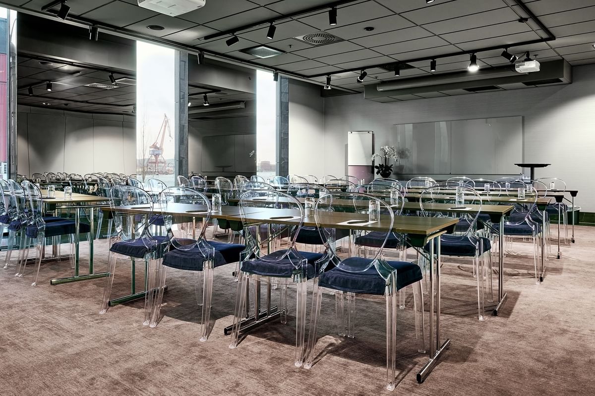 Rymlig konferenssal med kristallklara stolar och bord, belysning och panoramafönster med hamnvy.