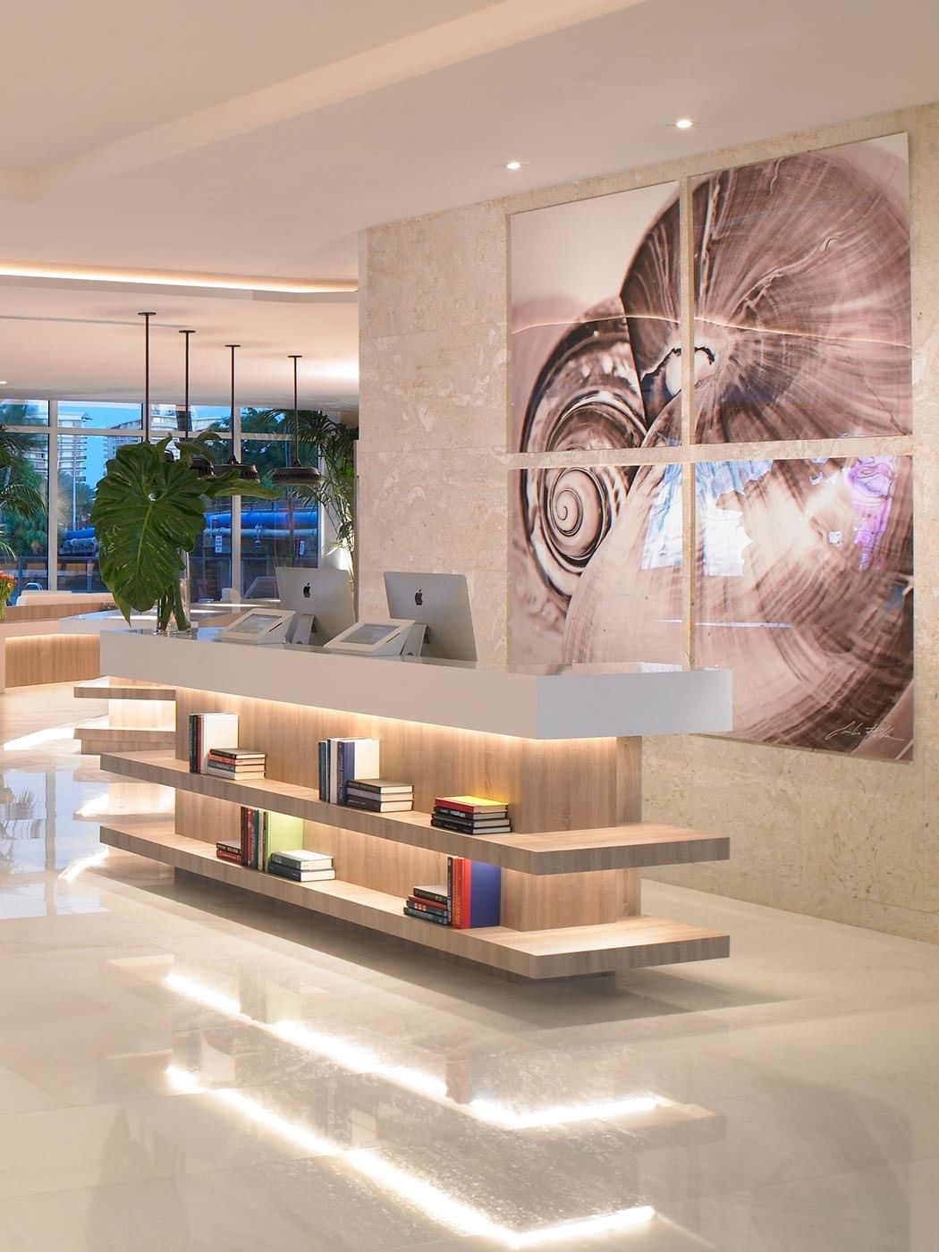A modern hotel lobby with a sleek reception desk, bookshelf, and artwork.