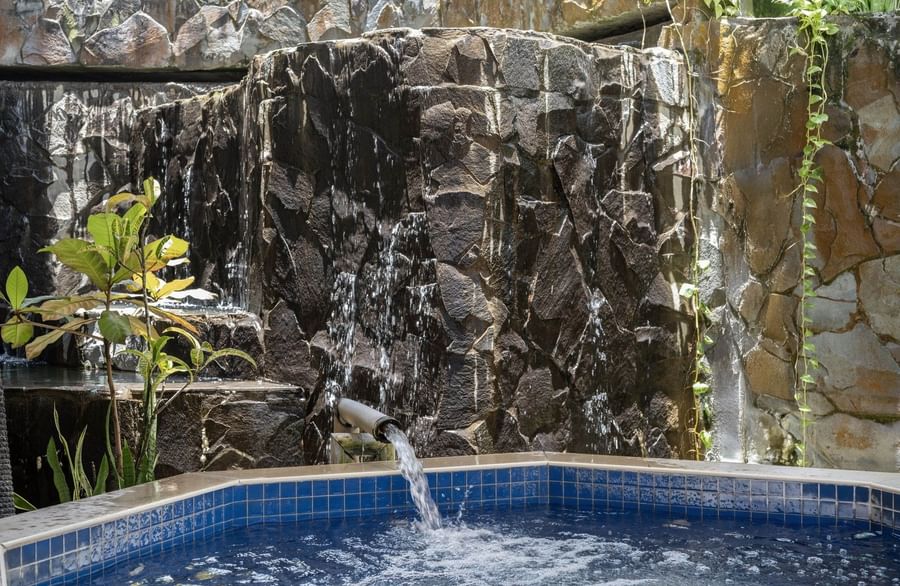 Blue tiled pool by a dark rock waterfall under green vines near a stone wall at Warwick Fiji Resort and Spa