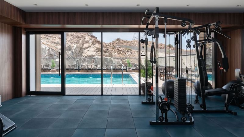 Modern gym with exercise equipment, with a glass door leading to a pool at Warwick Hotels and Resorts