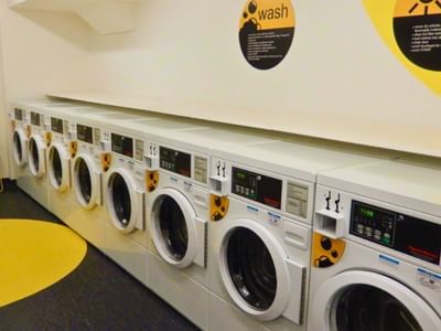 Row of white washing machines with yellow accents in a clean, well-organized laundry room.
