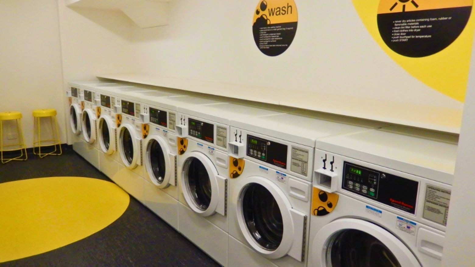 Row of white washing machines with yellow accents in a clean, well-organized laundry room.