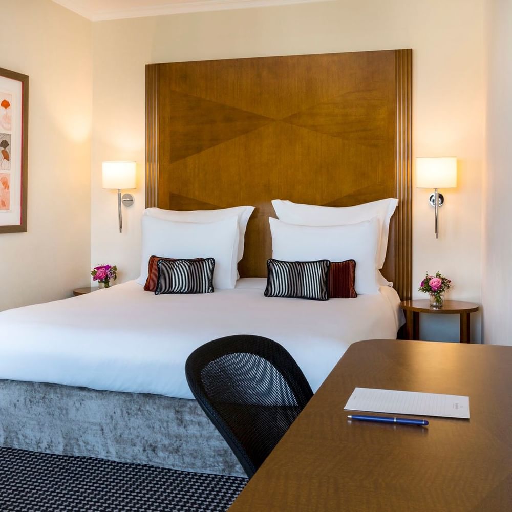 Plush hotel bed with a carved headboard, surrounded by framed art in Penthouse Executive Terrace Room at Warwick Geneva