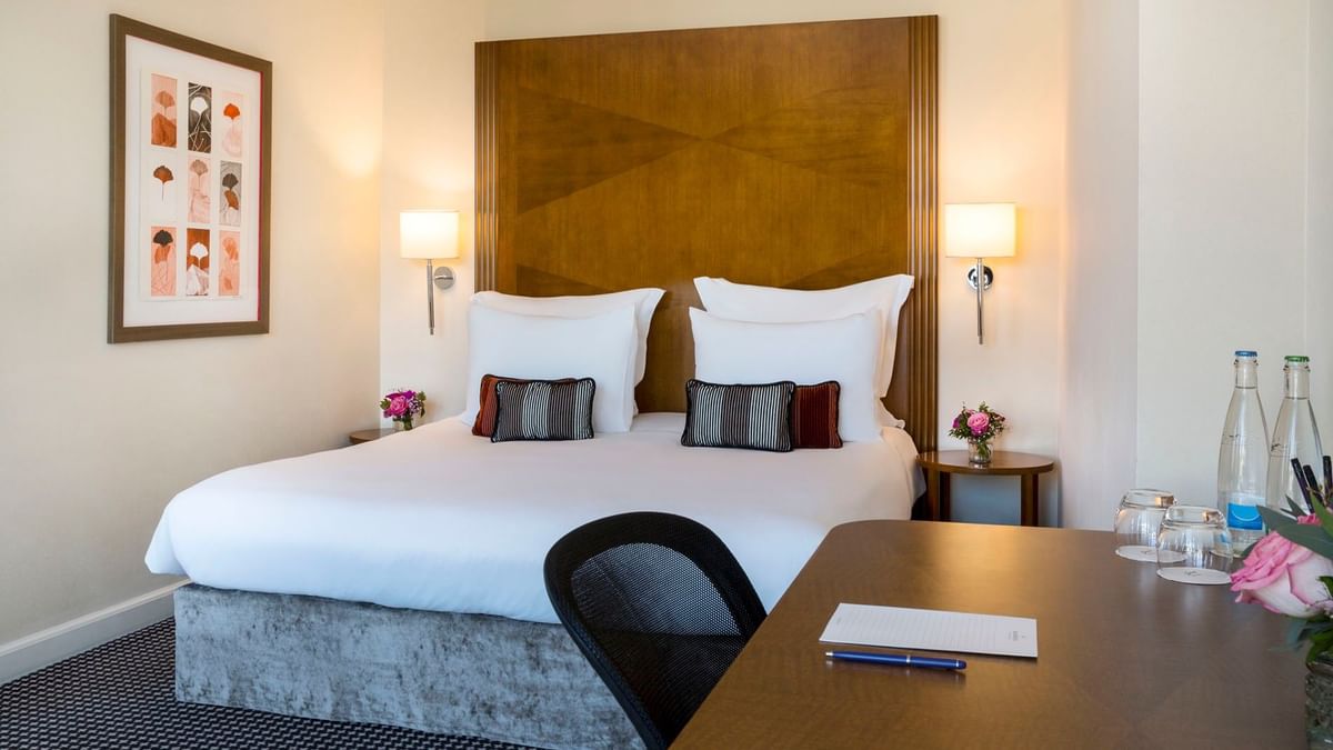 Plush hotel bed with a carved headboard, surrounded by framed art in Penthouse Executive Terrace Room at Warwick Geneva