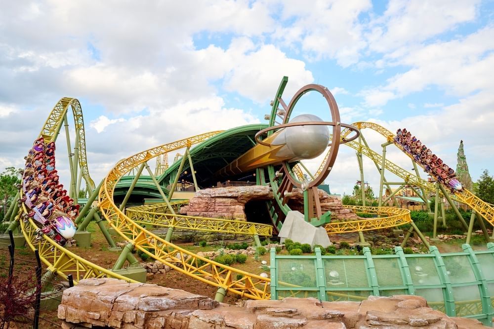Looping yellow roller coaster tracks and green walls wind around a large metal comet. 