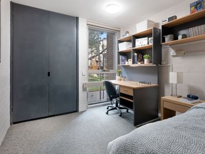 A clean student room with a bed, desk, chair, and shelves at La Trobe University – Menzies College.