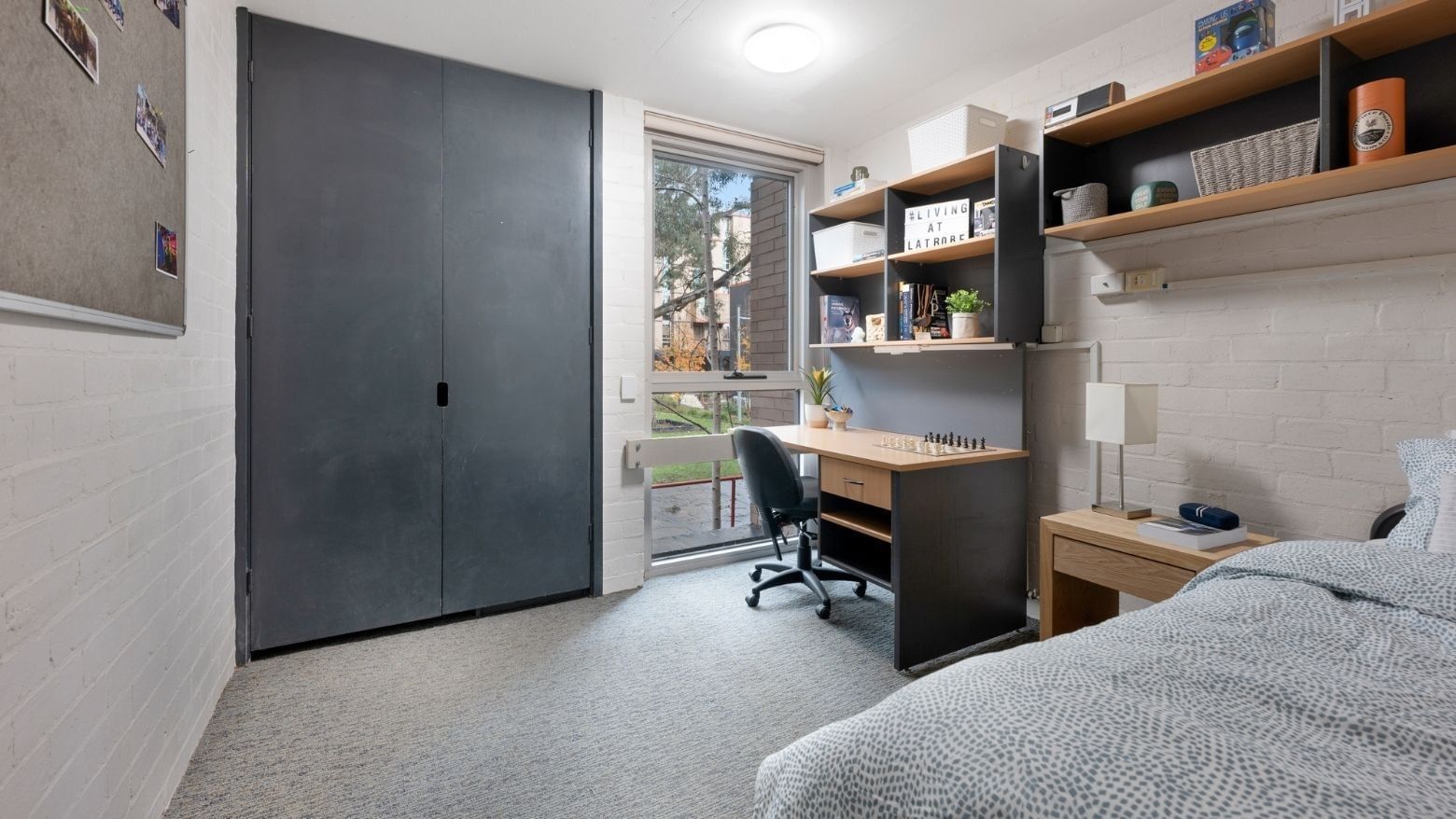 A clean student room with a bed, desk, chair, and shelves at La Trobe University – Menzies College.