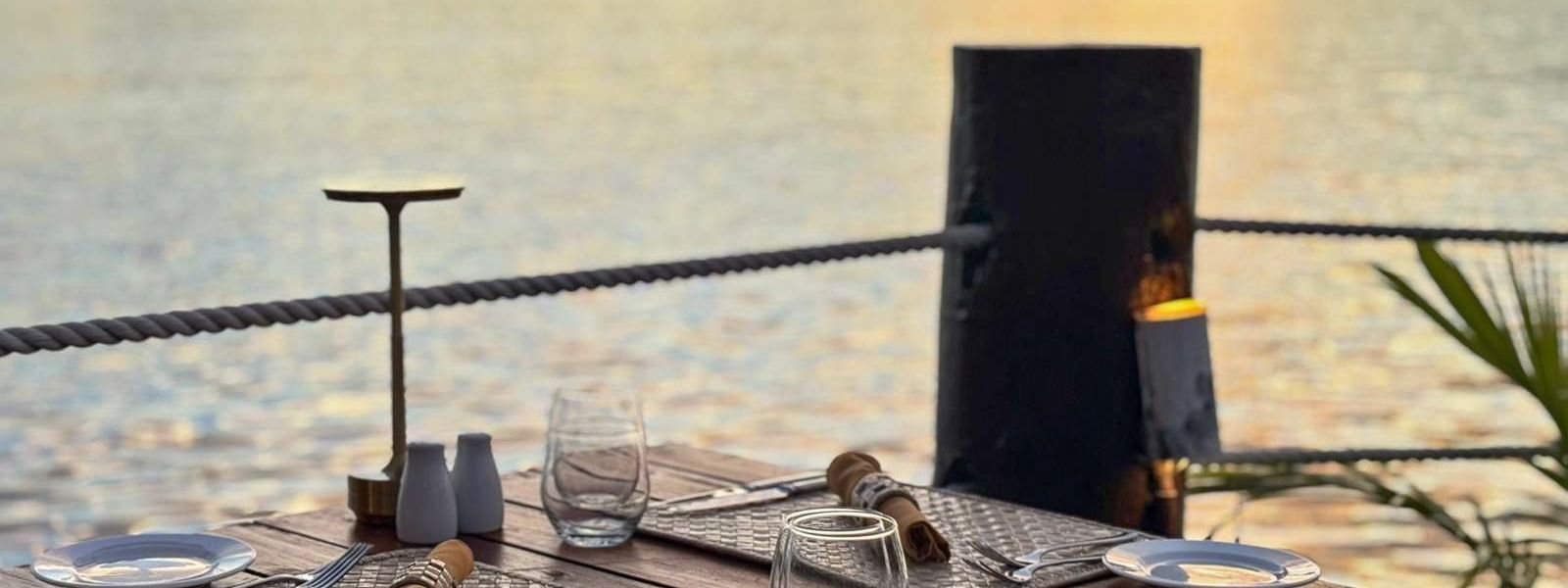 Dining table with woven mats by a rope railing under a sunset glow in Wicked Walu at Warwick Fiji Resort and Spa