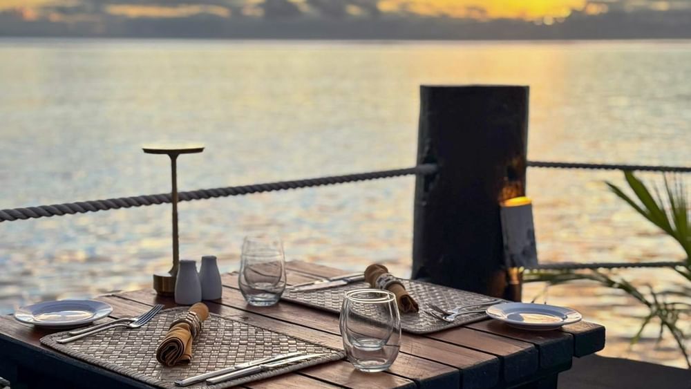 Dining table with woven mats by a rope railing under a sunset glow in Wicked Walu at Warwick Fiji Resort and Spa