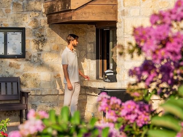 A guest at the stone-walled Turnhouse & Canteen window at Shangri-La Resort and Golf Club, framed by vibrant pink flowers