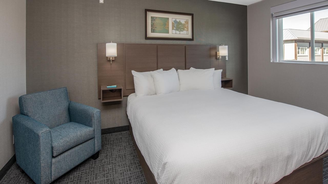 A suite bedroom with a bed, chair, and window.