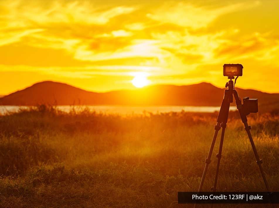 camera tripod set against a stunning mountain backdrop as it captures the sunset - Grand Lexis PD