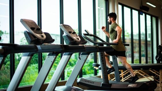 Man jogging on the treadmill in a bright gym with large windows showcasing greenery outside at Hotel des Innovations