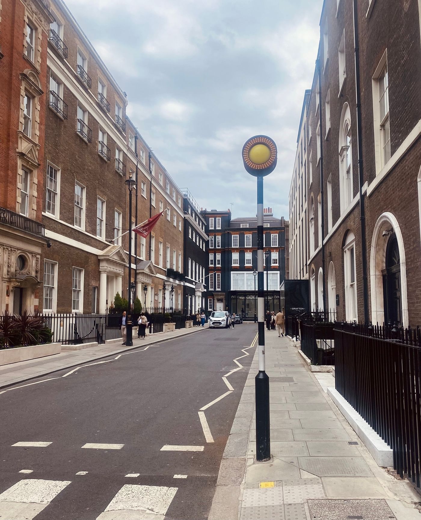 A charming street view of London with classic architecture, and a yellow circular streetlamp near The Londoner Hotel