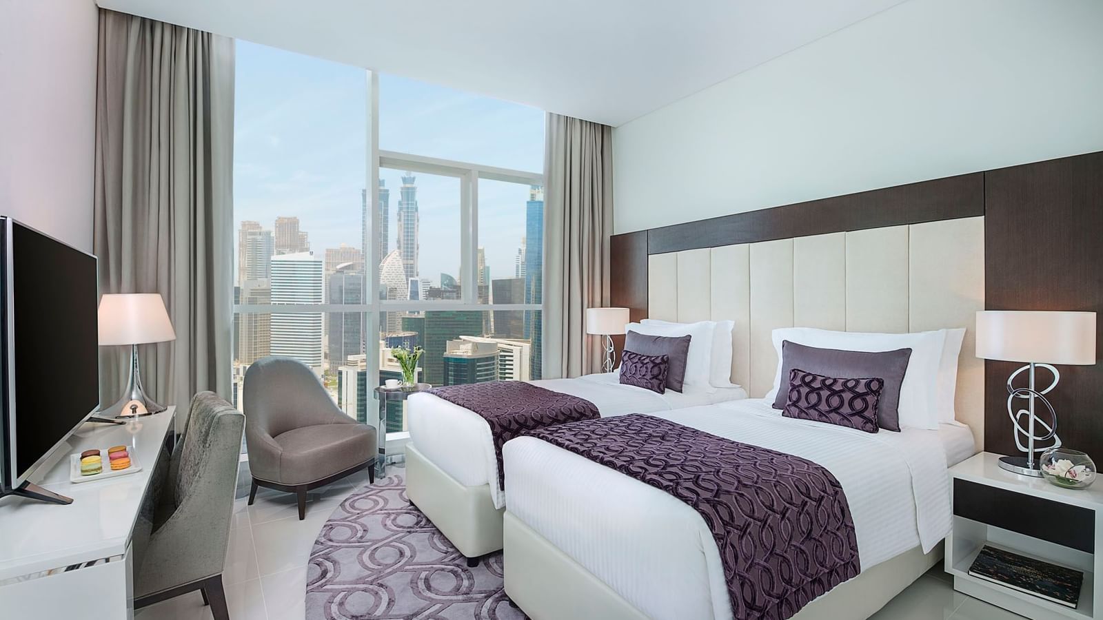 Twin beds by the window & a work desk with a chair in Three Bedroom Suite at DAMAC Maison Distinction