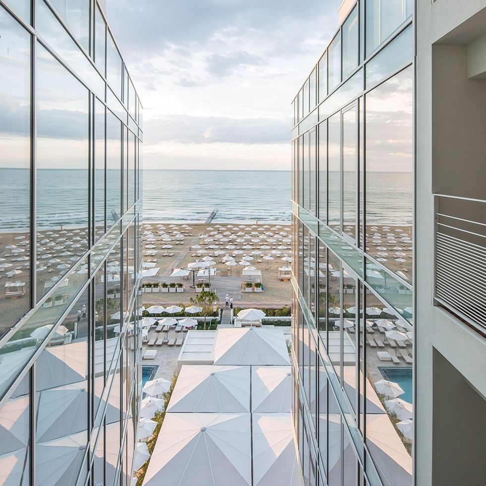 Falkensteiner Hotel & Spa Jesolo, with glass walls and terraces overlooking a beach with umbrellas and the ocean