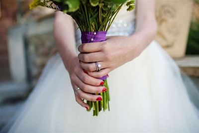 Close-up of a bride's hands holding a vibrant wedding bouquet with purple ribbon at The Ranch at Ucross