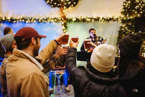 Cheerful festival crowds raising plastic cups under warm string lights at a rustic tavern layout at Oregon Garden Resort