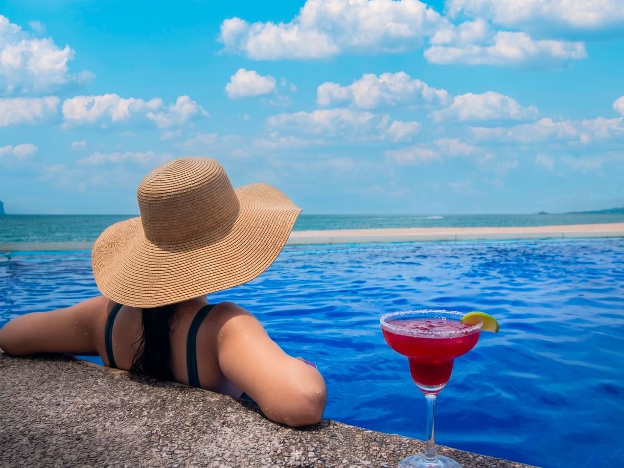 Woman relaxing by a pool with a drink for Cinco de Mayo offers.