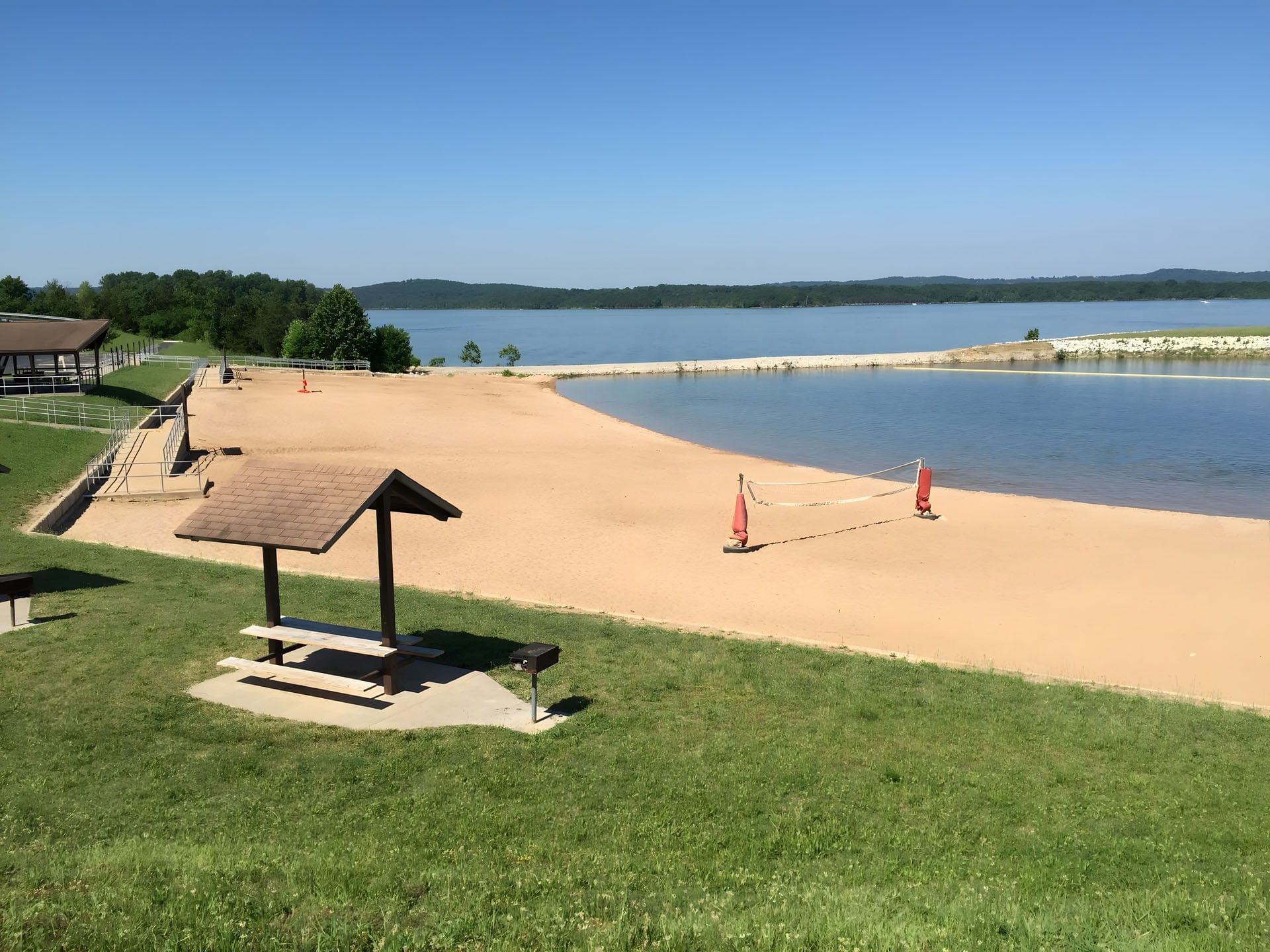Moonshine Beach area with a volleyball net, picnic shelter, and a wide view of a calm blue lake near Branson Hillside Hotel