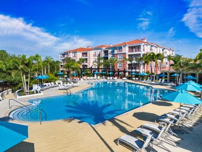 Resort pool area with umbrellas and lounge chairs in front of a multi-story building at Vista Cay Resort By Millenium