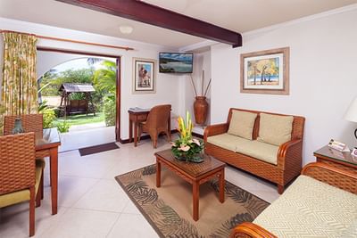 Wicker sofa and desk with wall-mounted TV looking out to a garden swing in Garden View Suite at Sugar Cane Club Hotel & Spa