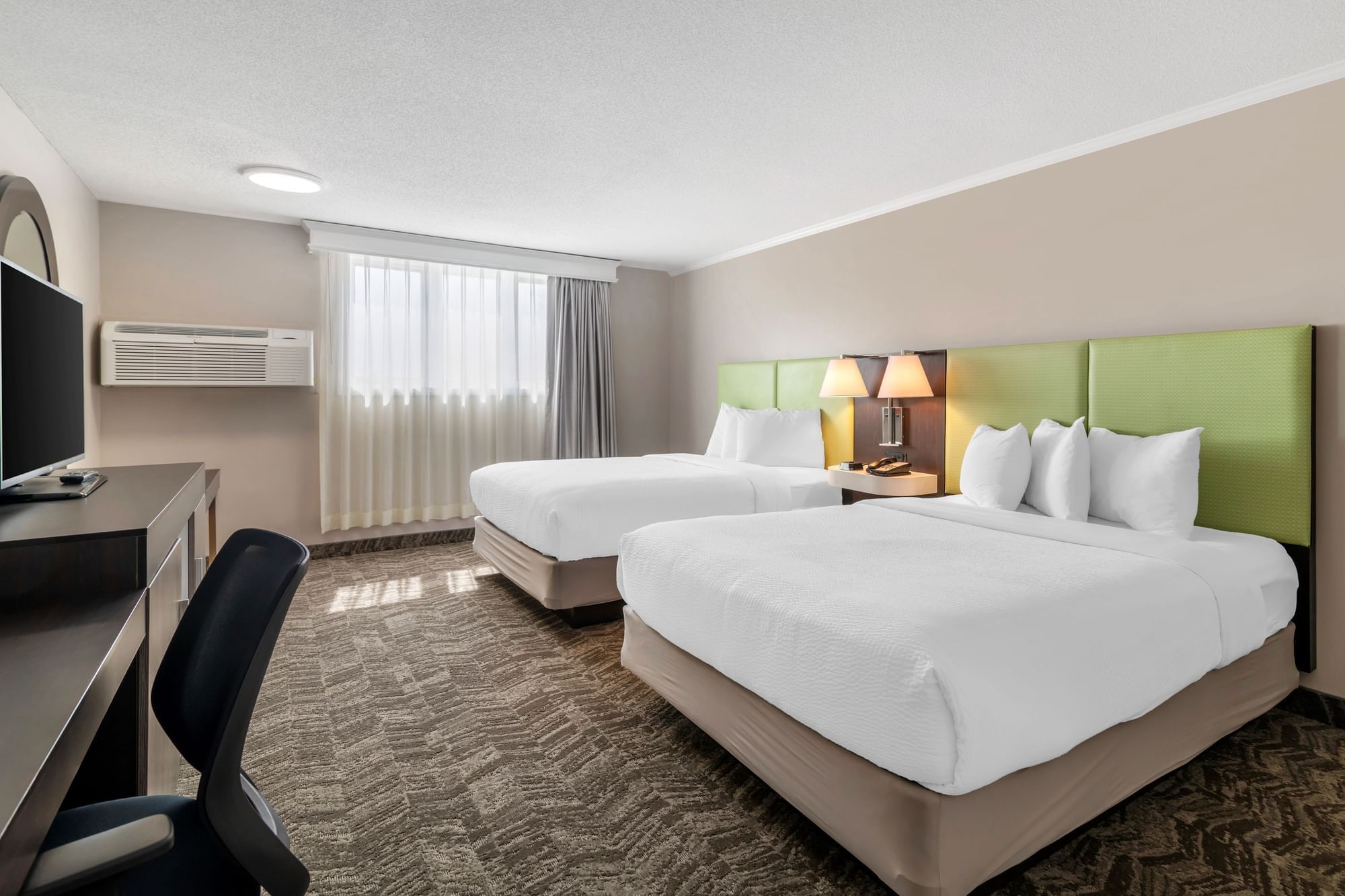 A hotel room with two queen beds, a desk, TV, and window.