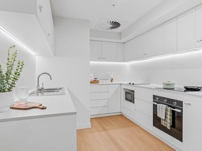 Modern kitchen with white cabinets, wooden floors, and sleek appliances at UniLodge Brisbane City.