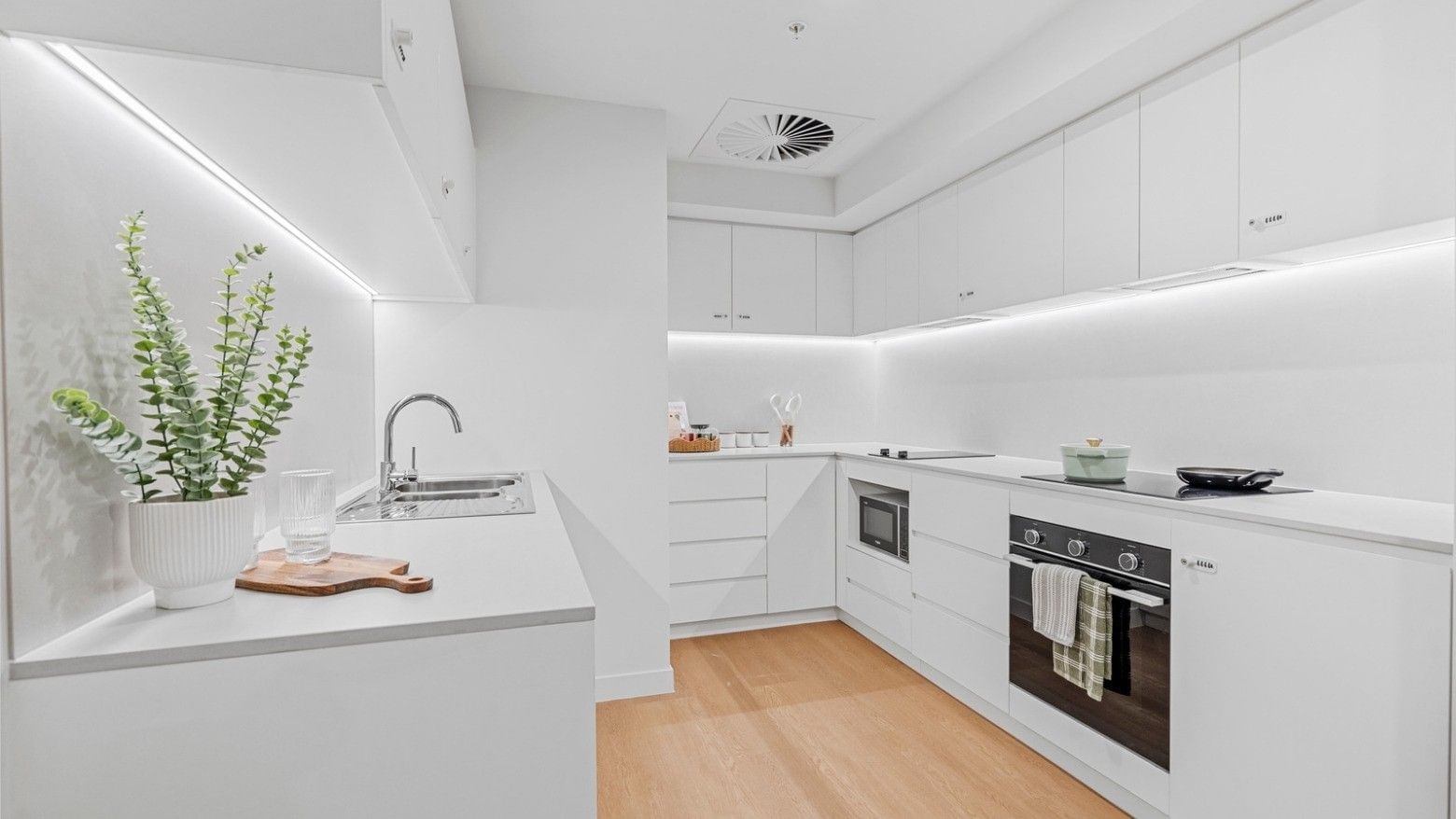 Modern kitchen with white cabinets, wooden floors, and sleek appliances at UniLodge Brisbane City.