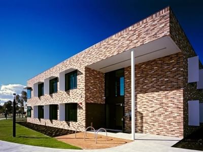 Modern brick building with a blue sky backdrop and a path leading to its entrance at La Trobe University.