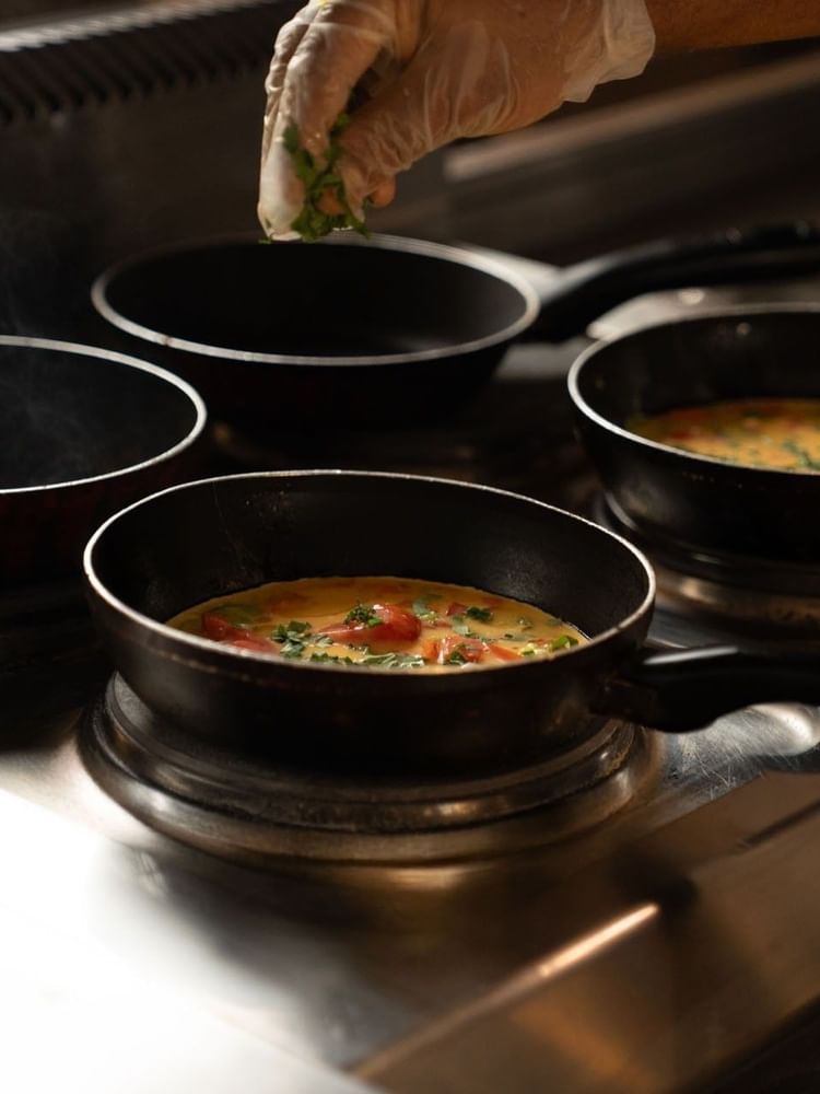 Chef adding fresh green herbs to several small pans of omelets cooking on a stove at Saja Warwick Madinah