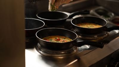Chef adding fresh green herbs to several small pans of omelets cooking on a stove at Saja Warwick Madinah