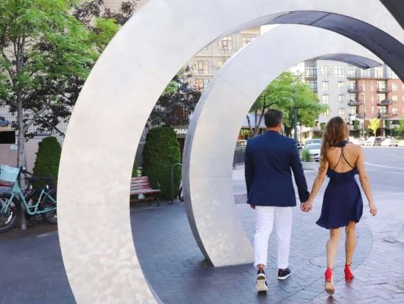 A couple strolling through a city sculpture while holding hands near Hotel 43