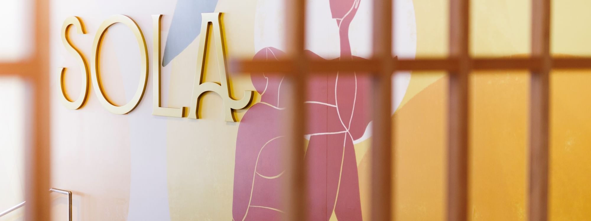 SOLA lettering on a pastel wall with abstract figures & wood accents in the Sola Bar at Novotel Sunshine Coast Resort hotel