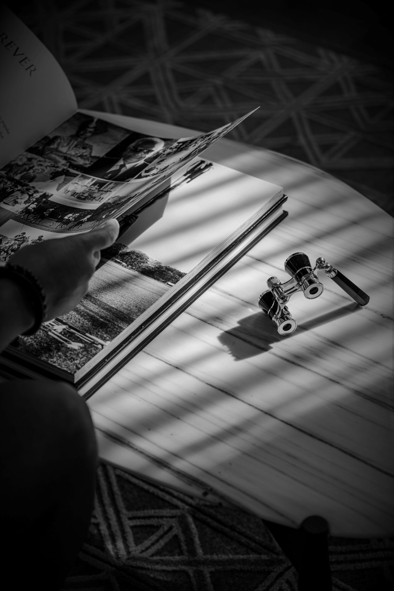 Black and white image of Authentic Models Opera Binoculars and a photo book displayed on a table at The Londoner