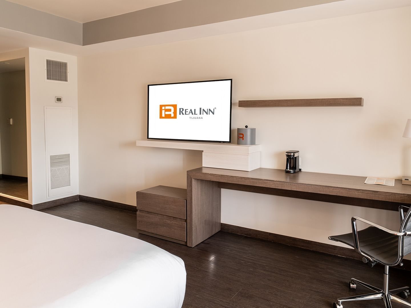Wall-mounted TV and work desk facing the cozy bed in the King Deluxe Room with wooden floors at Real Inn Tijuana