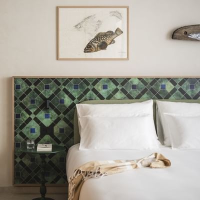 Camera da letto con testiera verde, libri, pesce dipinto e decorazioni geometriche.