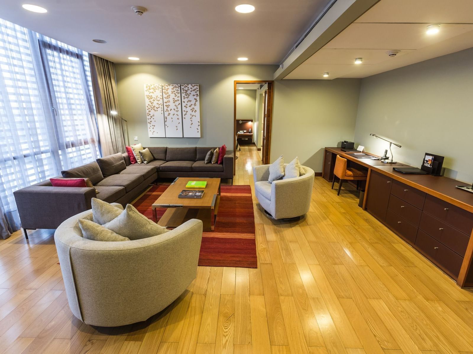 Sala de estar espaçosa da Executive Suite com sofá cinza, poltronas bege e piso de madeira no NOI Vitacura