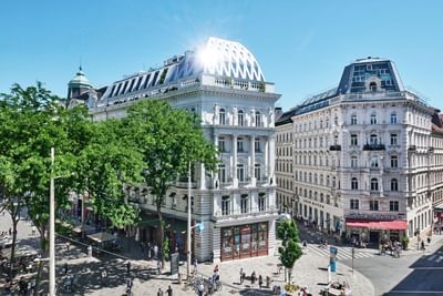 Exterior view of the grand Hotel Motto Vienna building on a sunny day, with people and trees