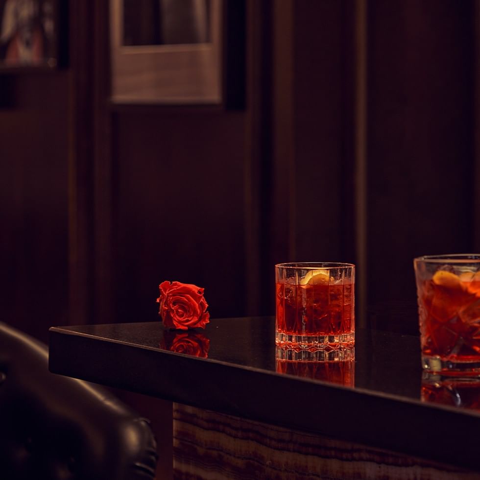 Due bicchieri di cocktail e una rosa rossa su un tavolo per Romantic Live Music Weekend.