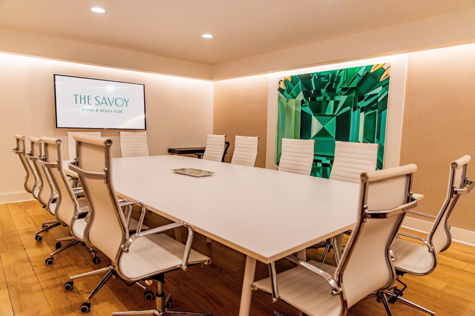 a conference room with a large white table, white chairs, a large screen on the wall, and a green abstract art piece