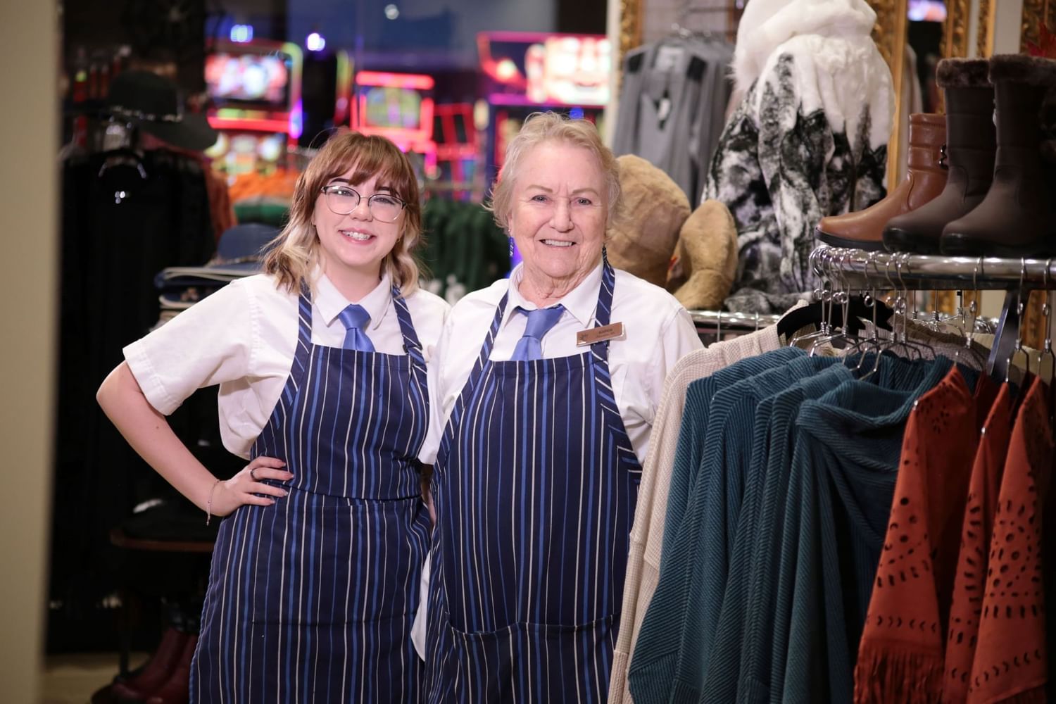 Two smiling female retail staff members in striped aprons standing near clothing displays at Eureka Casino Resort