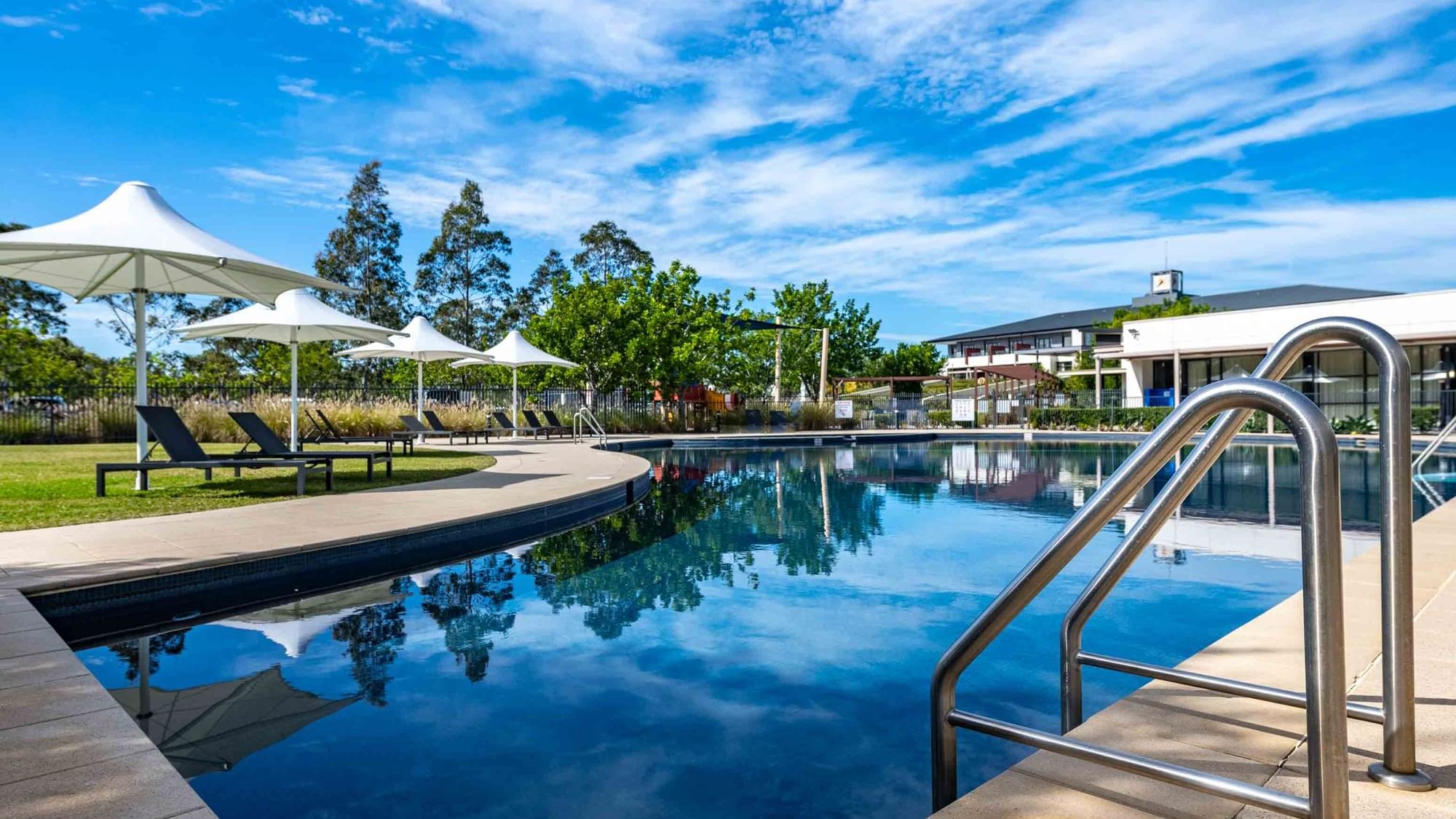 Outdoor pool with sun loungers and white parasols at Mercure Kooindah Waters