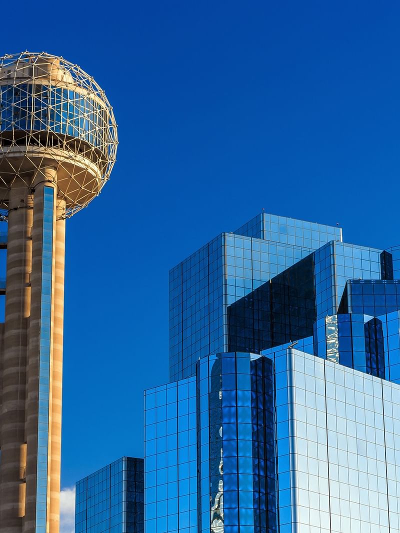 Reunion Tower and a tall glass building against a blue sky.
