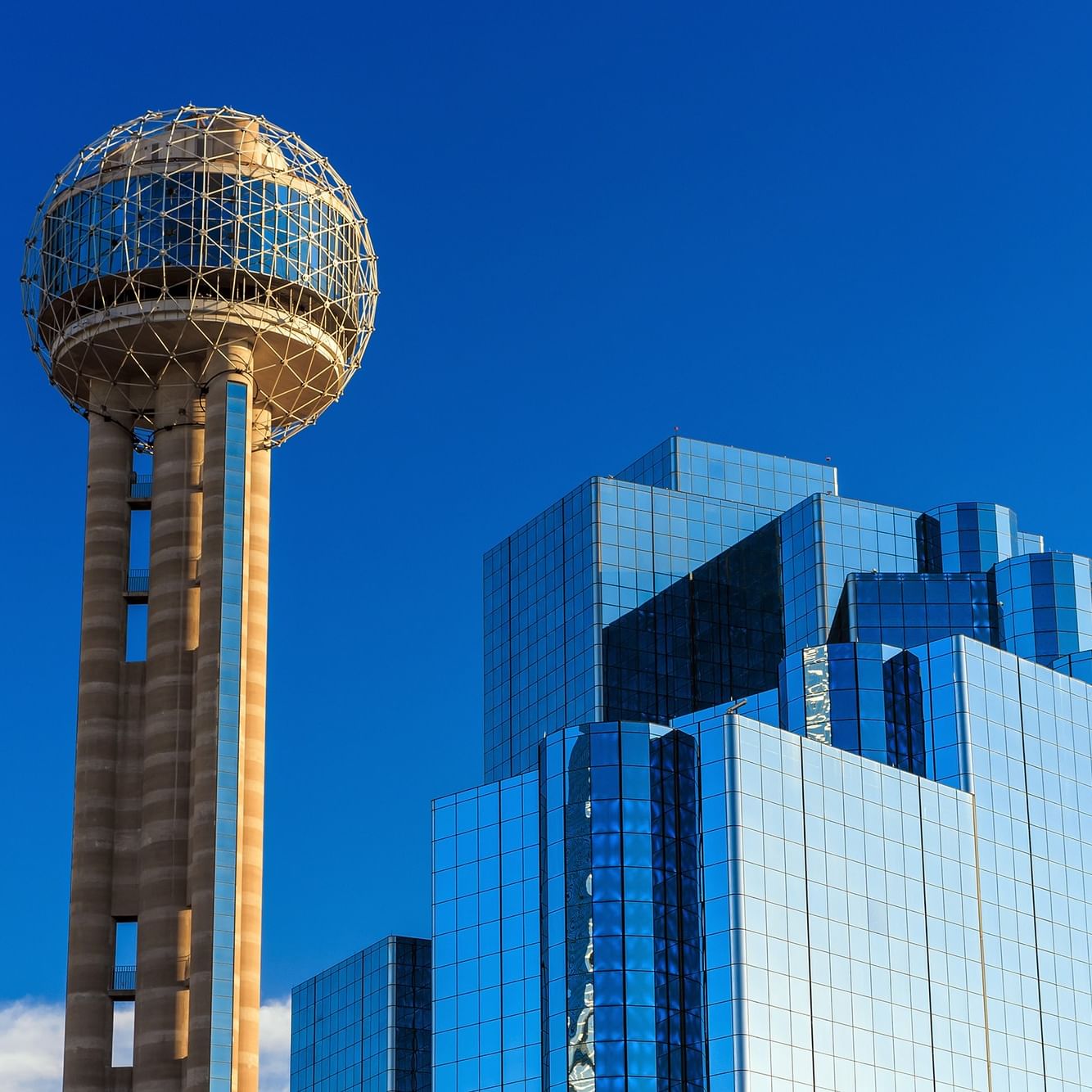 Reunion Tower and a tall glass building against a blue sky.