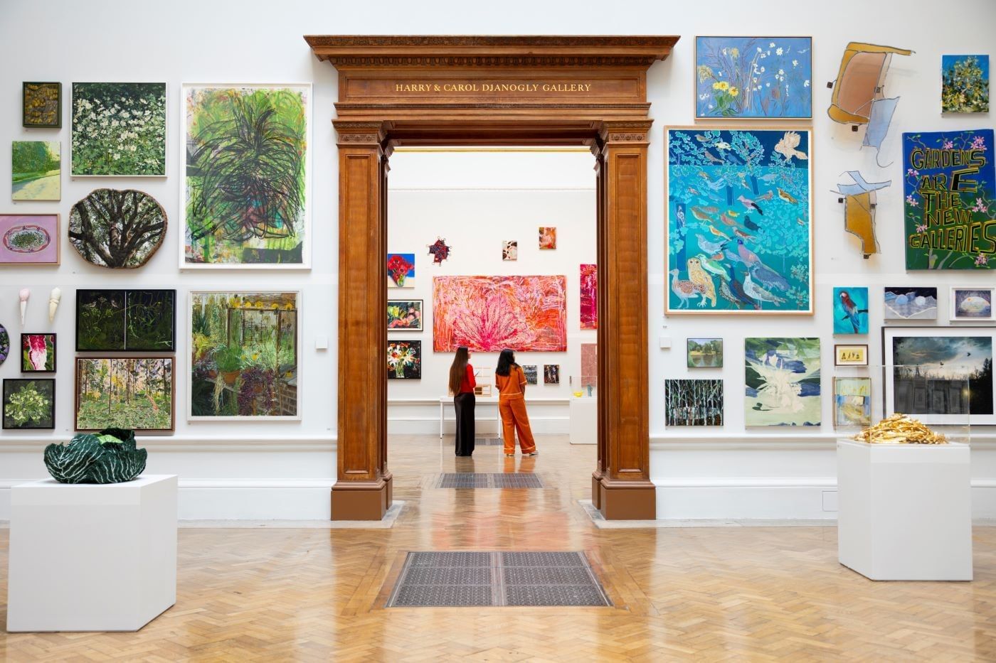 Two visitors viewing colorful artwork through an ornate wooden doorway at the Royal Academy of Arts for the summer exhibition