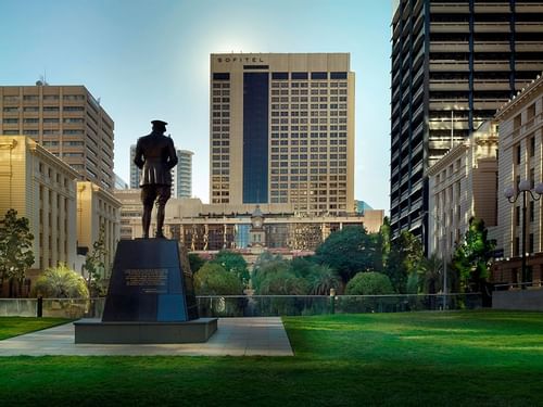 Statue in a park with high-rise buildings, including a Sofitel Brisbane Central hotel, in the background