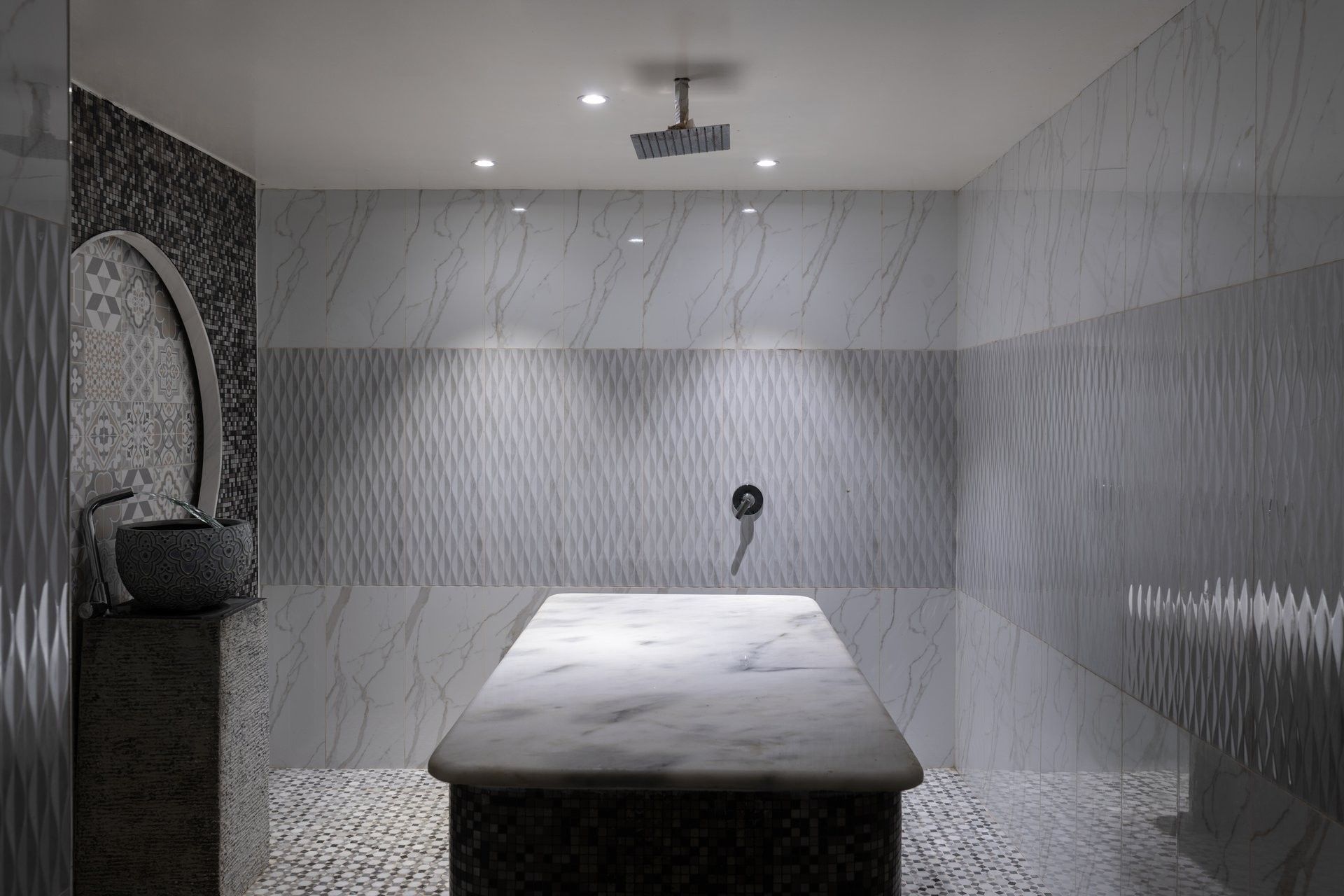 Marble scrub table by a stone basin under a rain shower head in Golden Time Spa at Warwick Al Taif Hotel