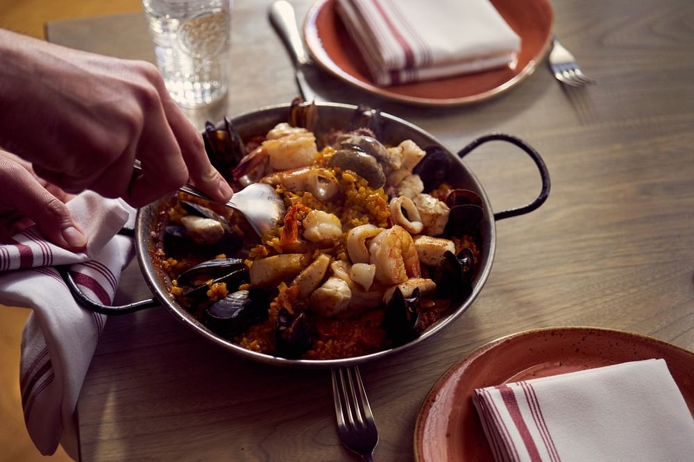 Seafood paella in a pan by striped napkins and a glass of water on a table at Warwick San Francisco