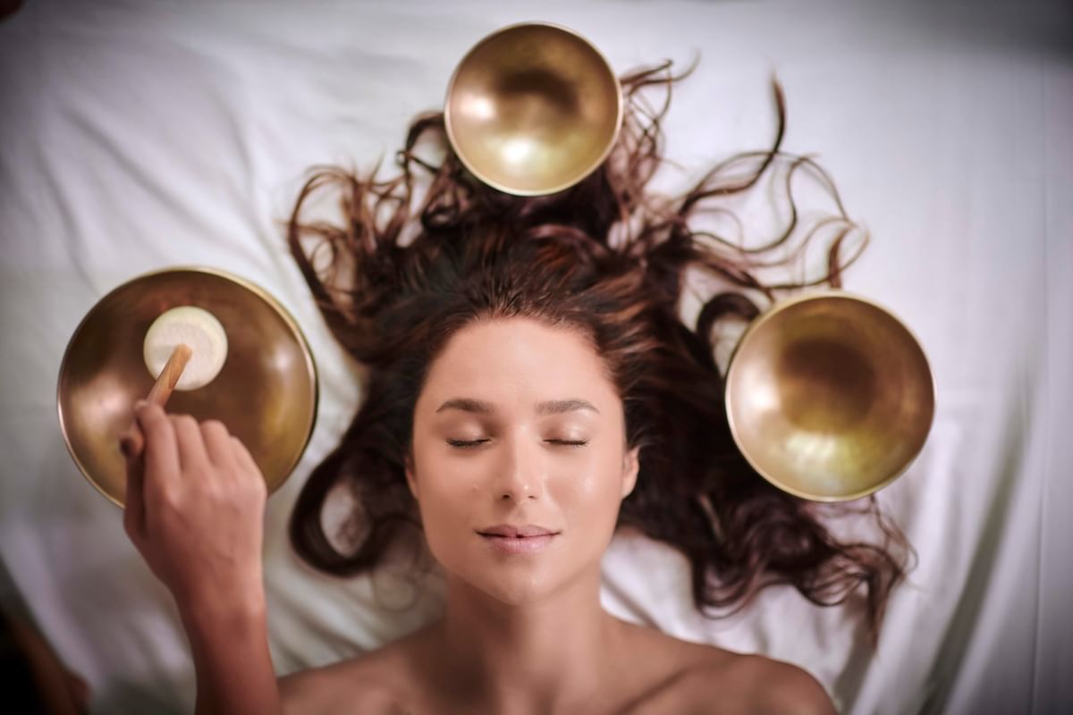 Woman enjoying a meditative sound bath with golden bowls in Lahari Wellness Center at Cala Luna Boutique Hotel